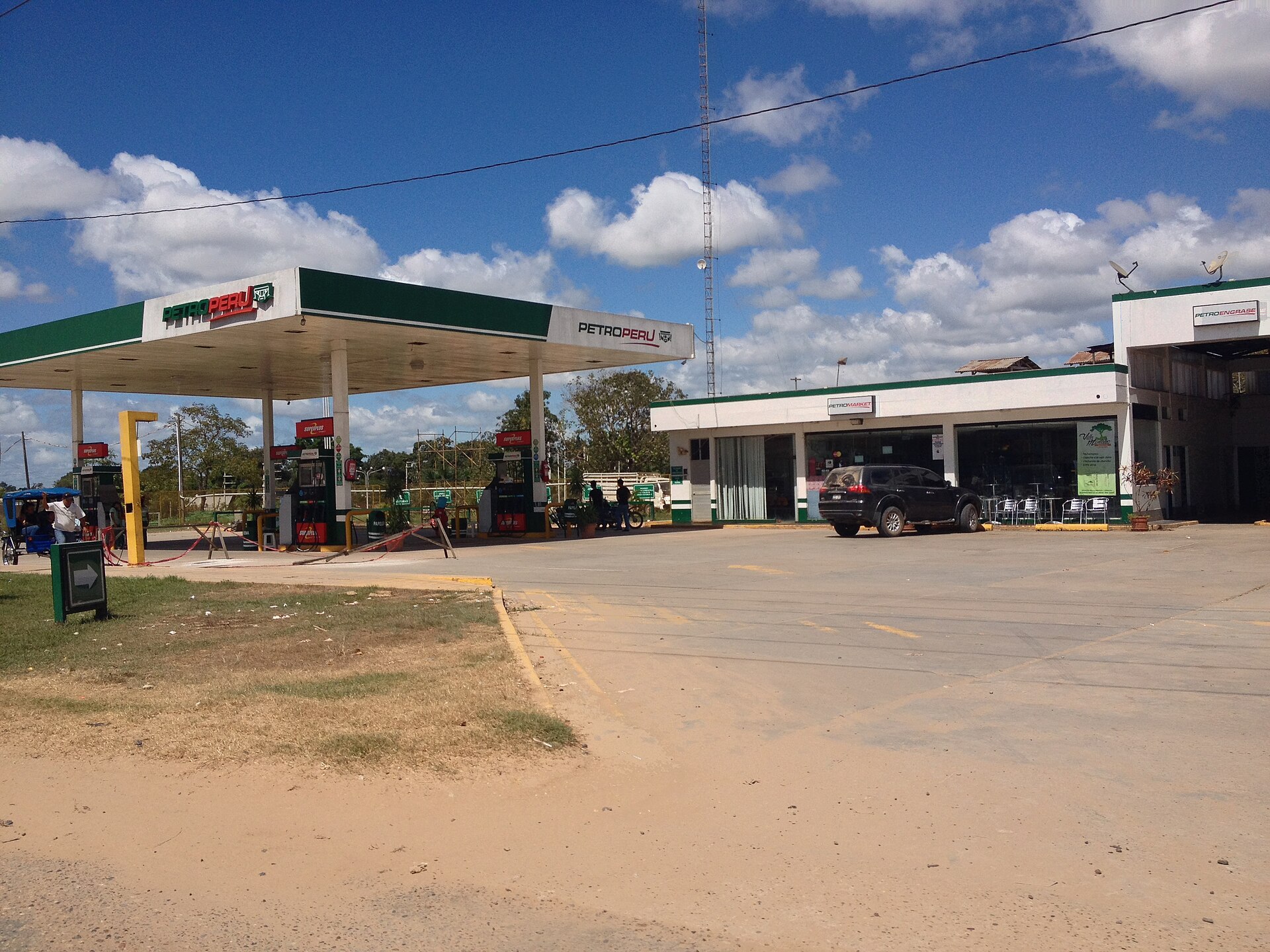 A Petroperu fuel station with a green and white canopy and a shop building under a blue sky, with a dirt forecourt in front
