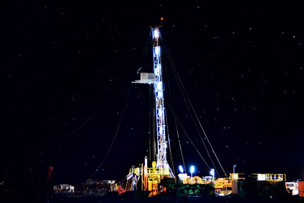 A lit drilling rig stands against a starry night sky at an oil field site