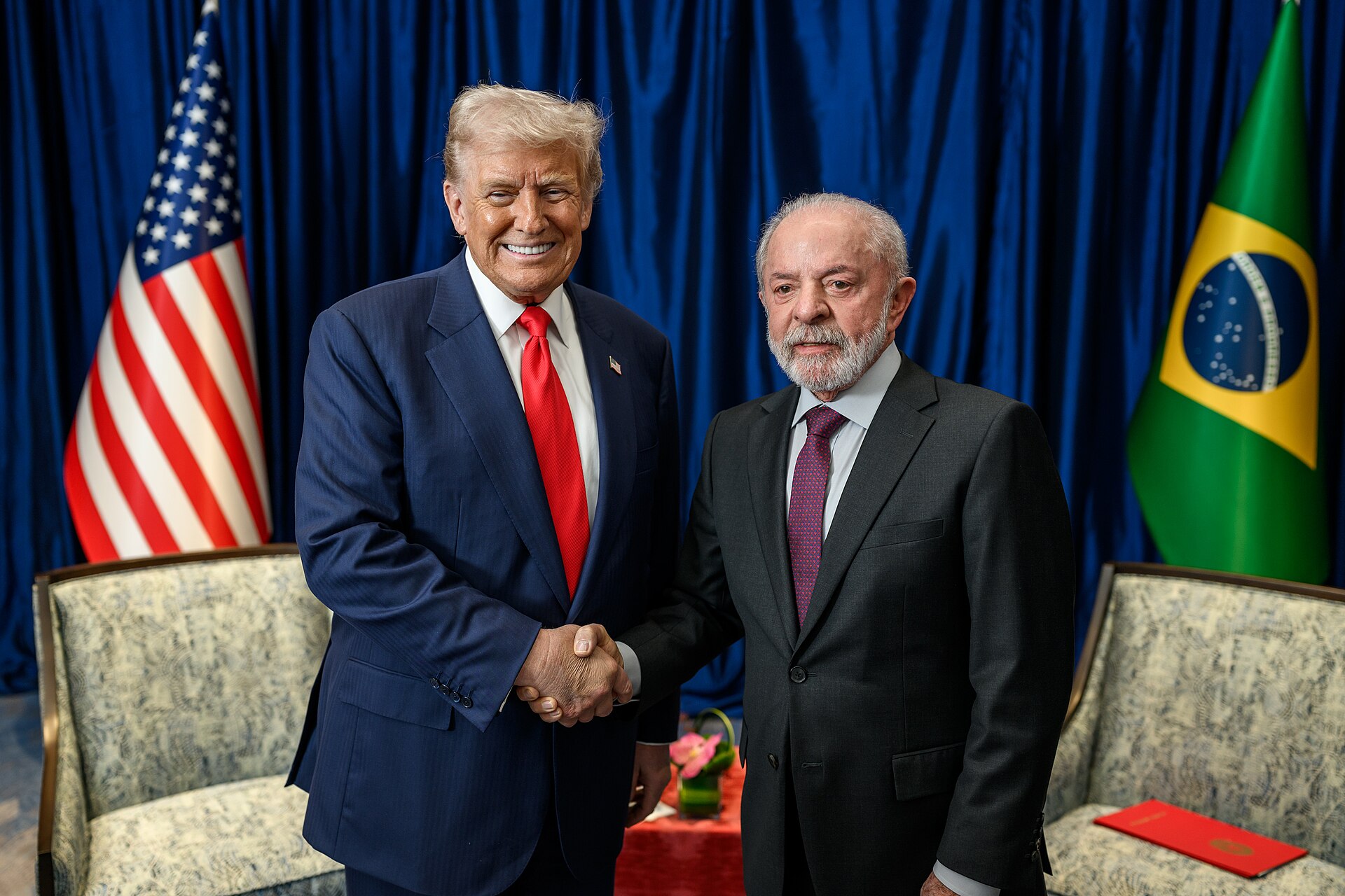 Donald Trump and Lula shake hands in front of US and Brazilian flags