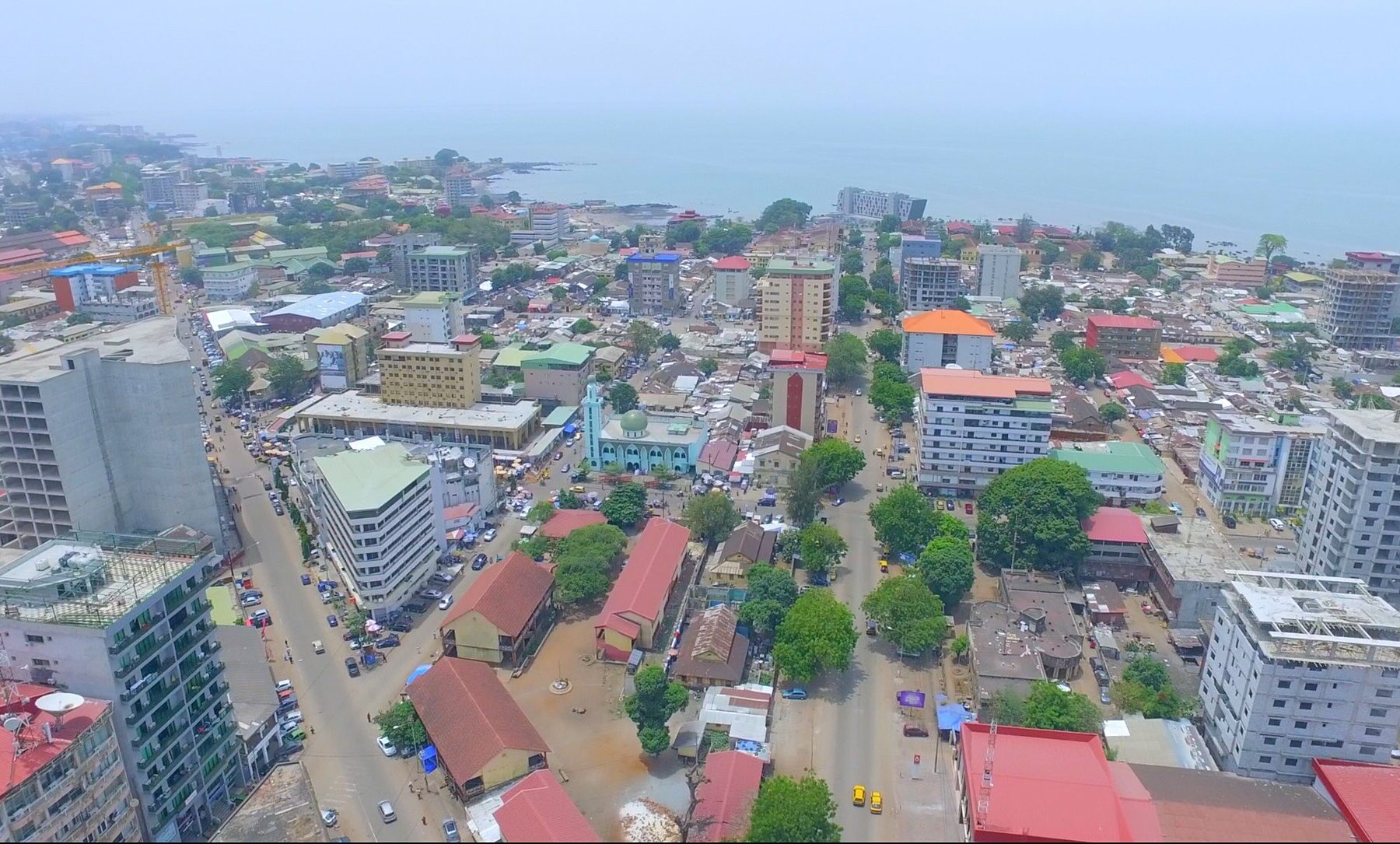 Aerial view of central Conakry with apartment blocks, red roofs, tree-lined streets and the Atlantic coast in the distance
