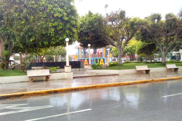 Central plaza in Nagua, Dominican Republic, with colourful letters spelling the town's name, trees, benches and a wet street