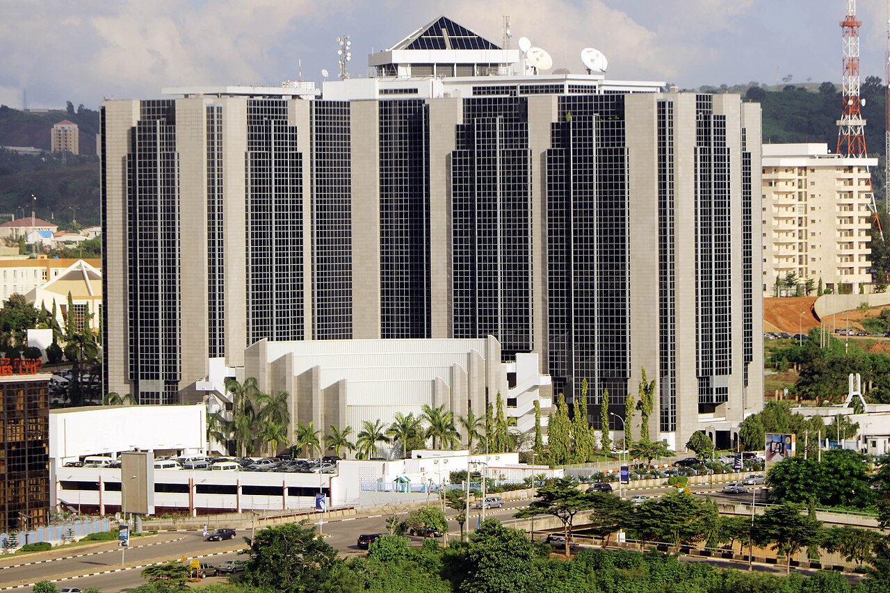 The Central Bank of Nigeria headquarters, a dark-glass tower block with palm trees in front, in Abuja