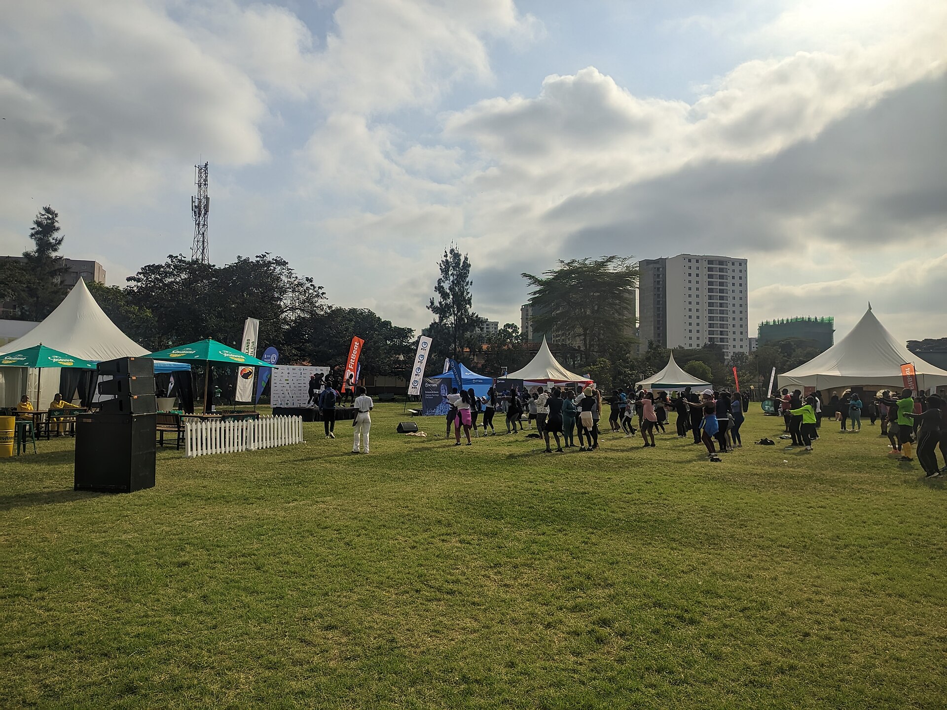 Runners in a group workout on the lawn at Parklands Sports Club in Nairobi during a Standard Chartered Nairobi Marathon warm-up event, with tents and apartment towers behind