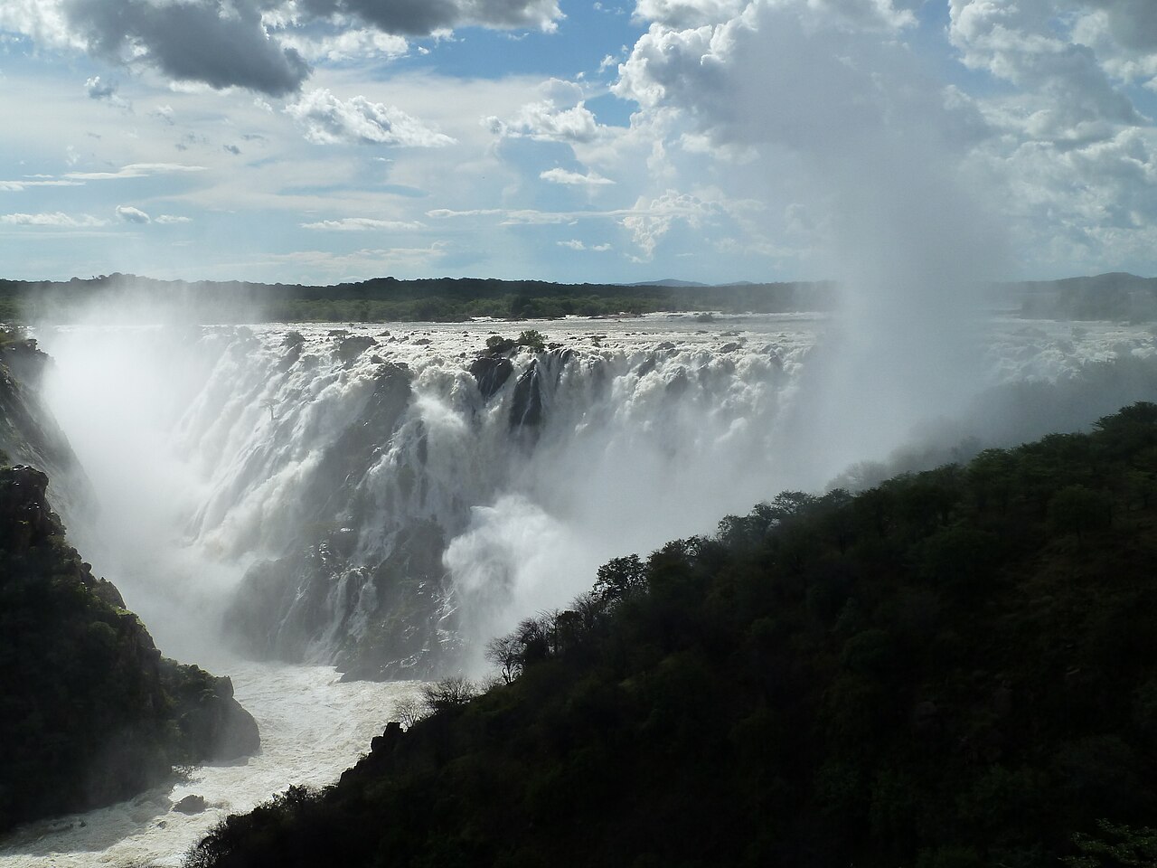 Ruacana Falls on the Kunene River, a wide curtain of white water falling into a green gorge under a cloudy sky