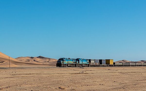 Cargo train with blue locomotives crossing the desert near Walvis Bay, Namibia, with sand dunes behind