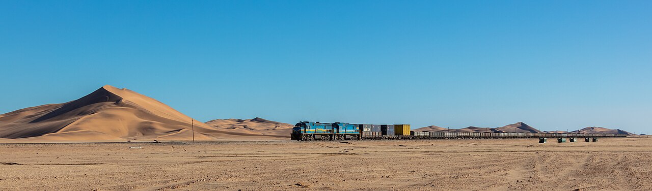 Cargo train with blue locomotives crossing the desert near Walvis Bay, Namibia, with sand dunes behind