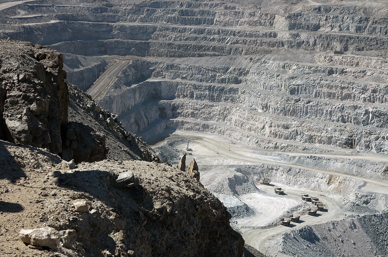 Terraced walls of the open-pit Rössing uranium mine in the Namib desert, with a line of haul trucks on the pit floor.