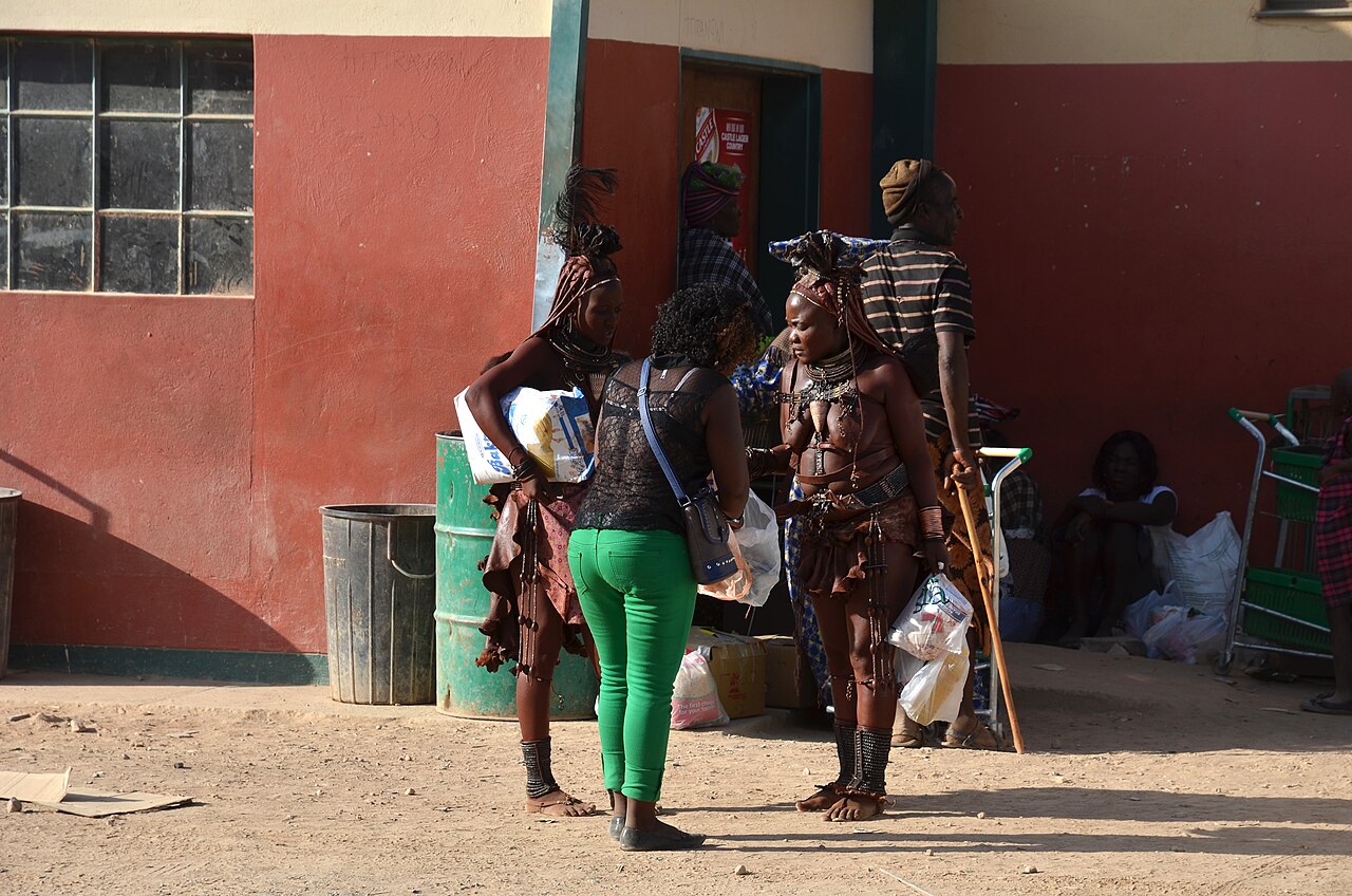 Two Himba women in traditional dress holding shopping bags outside a shop in Opuwo, Namibia