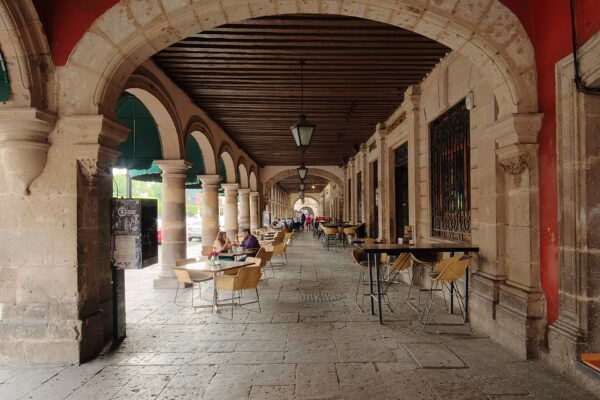 A stone arcade with wooden beams and lanterns in the historic centre of Morelia, with people seated at cafe tables