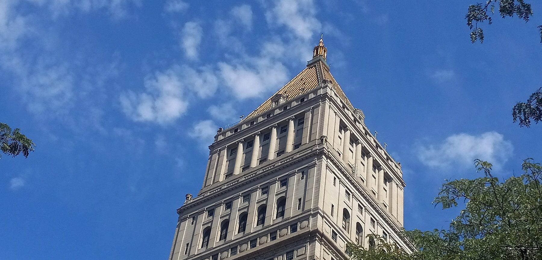 The pyramid-topped tower of the Thurgood Marshall United States Courthouse in Lower Manhattan against a blue sky with trees at the edges