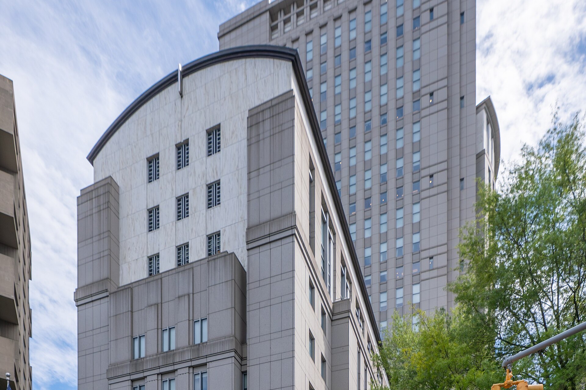 The granite Daniel Patrick Moynihan United States Courthouse tower and entrance at the corner of Worth and Baxter Streets in Manhattan under a cloudy blue sky
