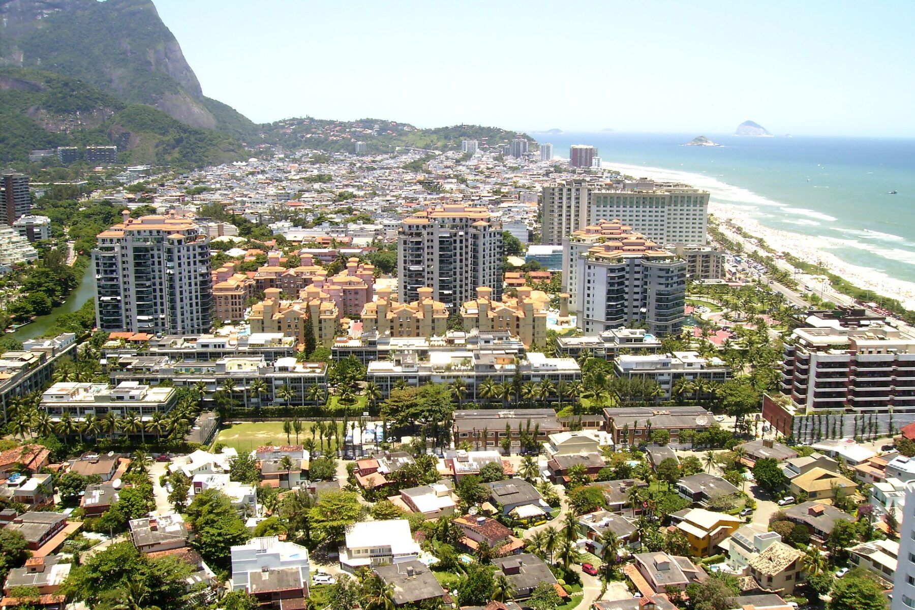 Aerial view of Barra da Tijuca in Rio de Janeiro with apartment towers, low houses, a beach on the right and a green granite peak at the left