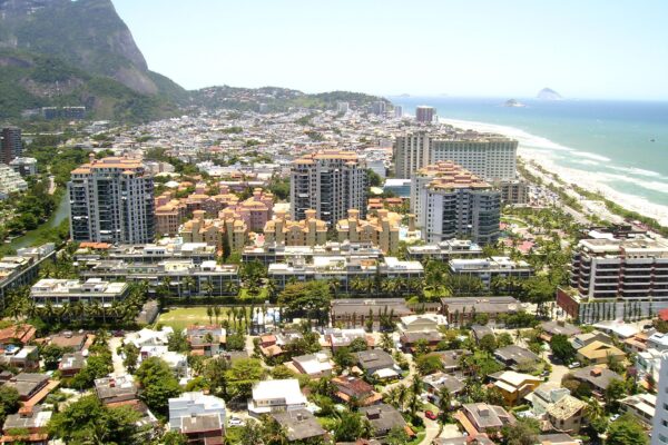 Aerial view of Barra da Tijuca in Rio de Janeiro with apartment towers, low houses, a beach on the right and a green granite peak at the left