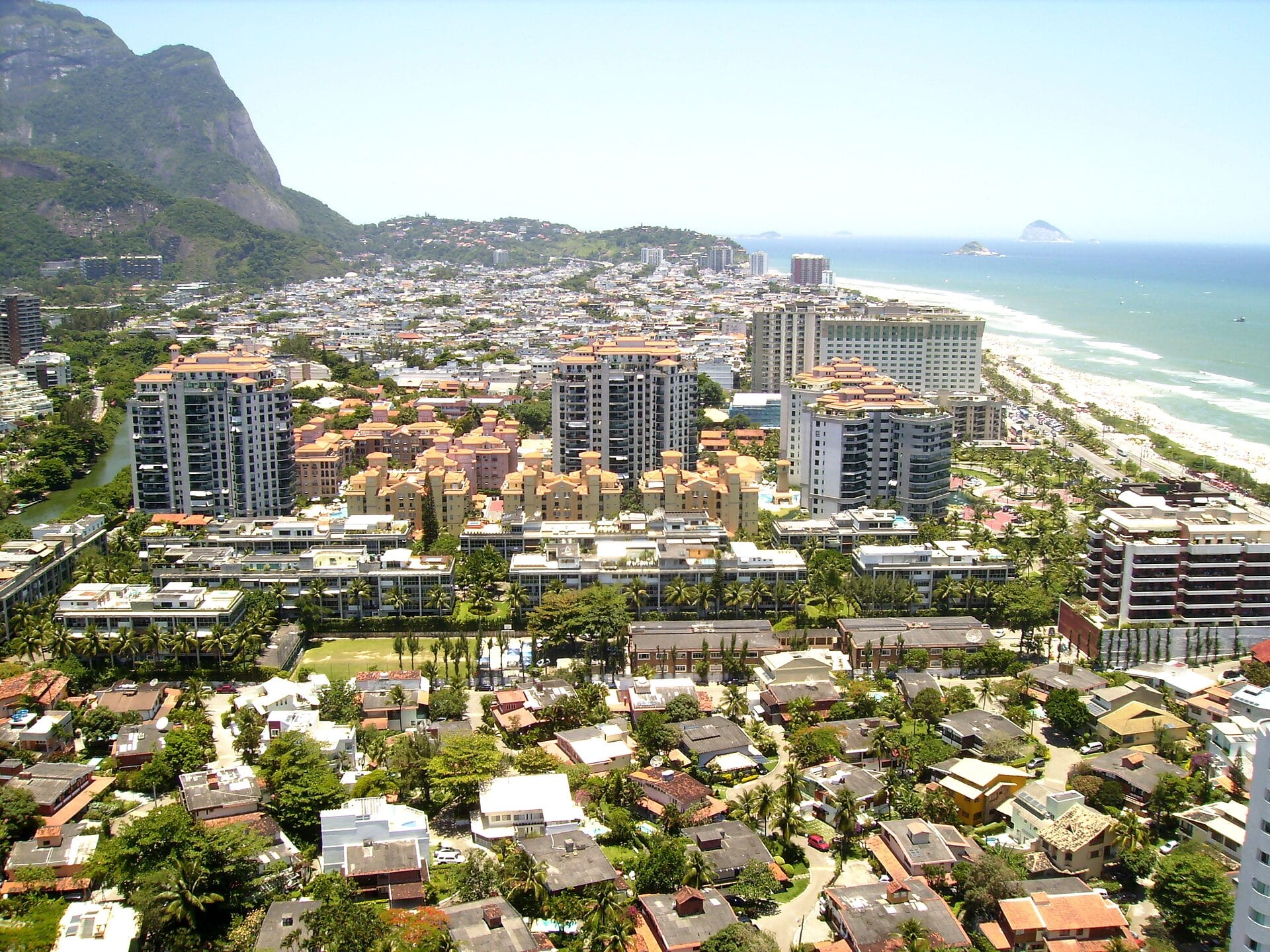 Aerial view of Barra da Tijuca in Rio de Janeiro with apartment towers, low houses, a beach on the right and a green granite peak at the left