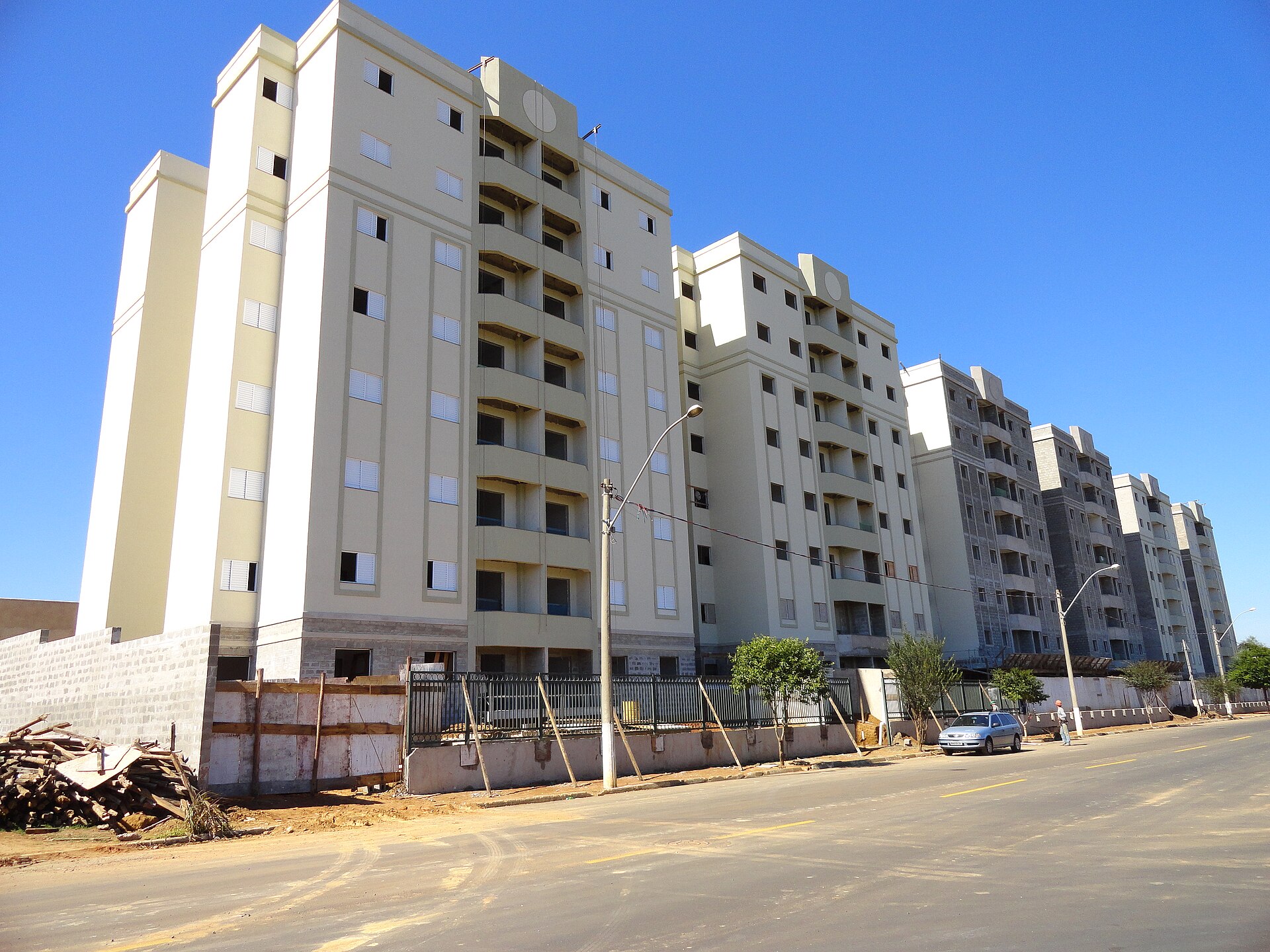 A row of beige and grey apartment blocks, some still under construction, beside a road under a blue sky