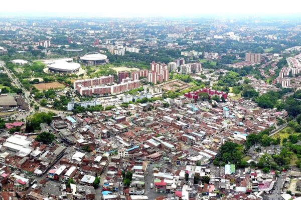 Aerial view of Cali, Colombia, with sports arenas and apartment blocks beyond dense low-rise neighbourhoods and a green hill