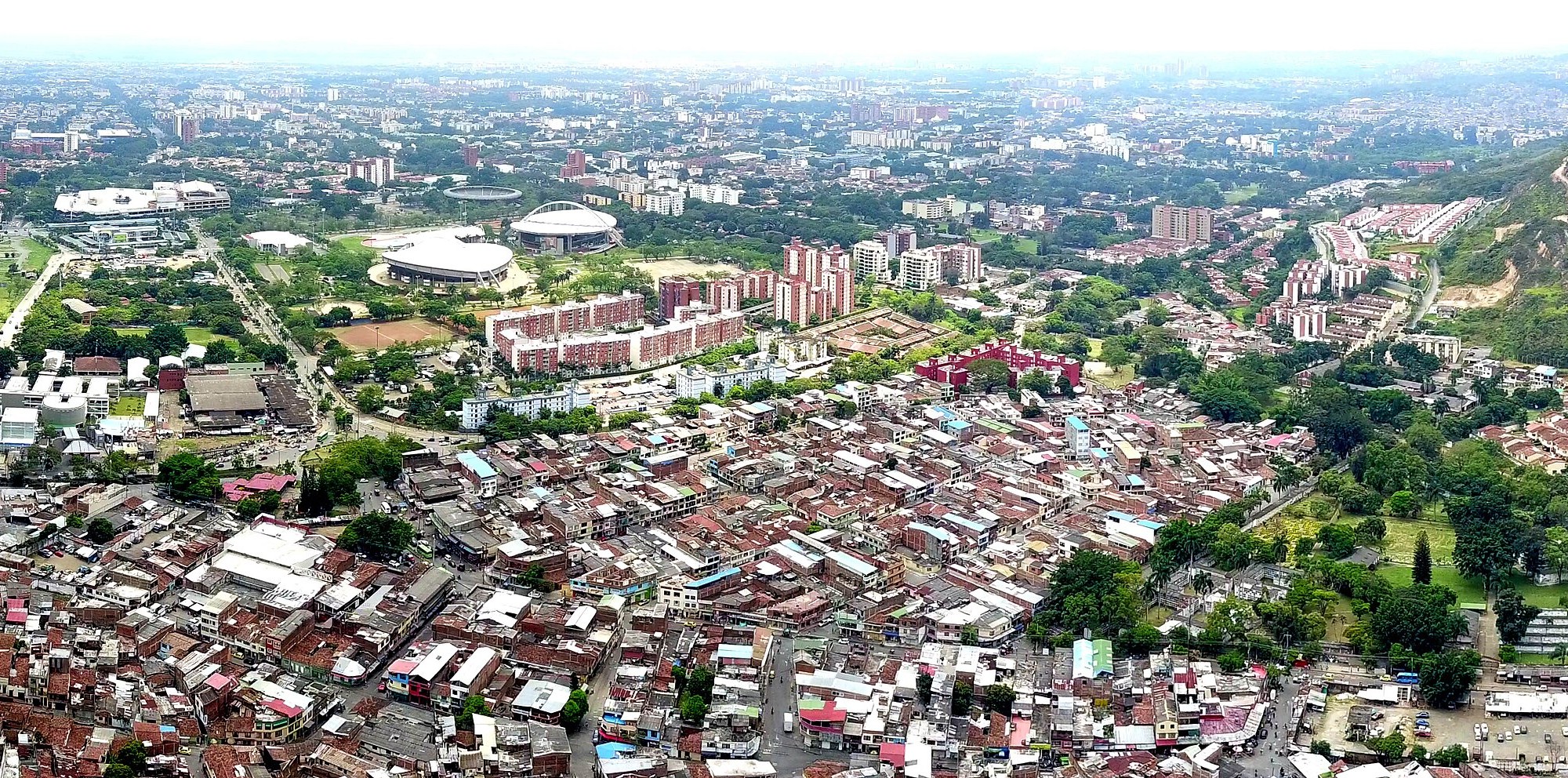 Aerial view of Cali, Colombia, with sports arenas and apartment blocks beyond dense low-rise neighbourhoods and a green hill