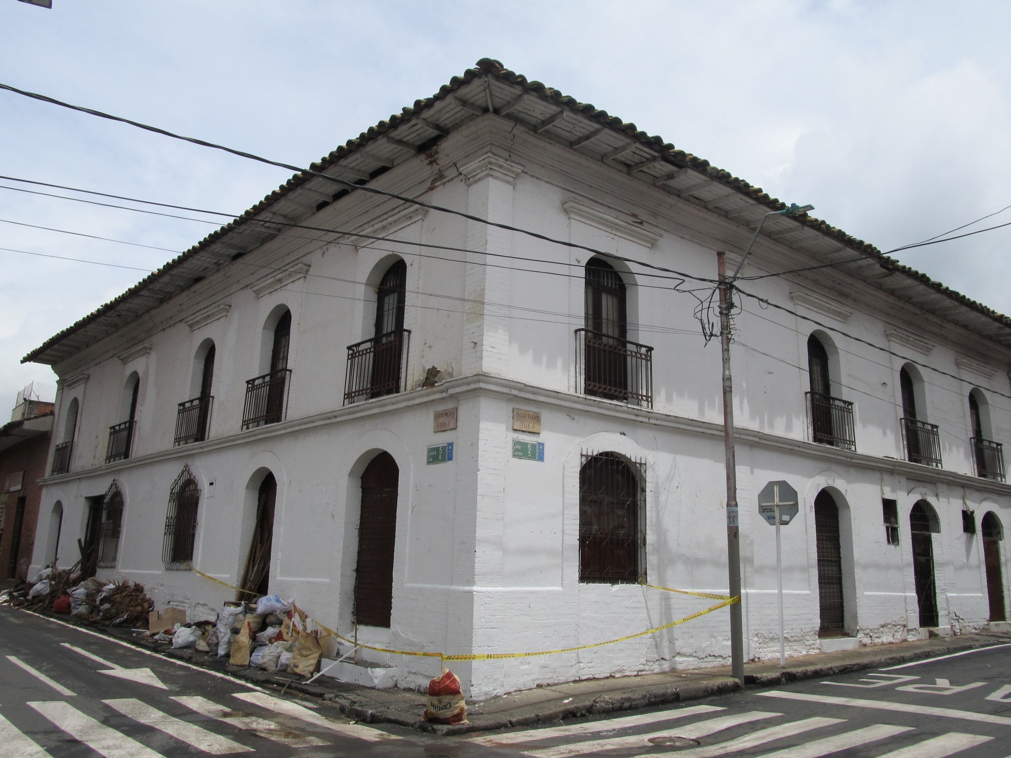 White two-storey corner building with arched windows and balconies, taped off, with rubble bags on the pavement