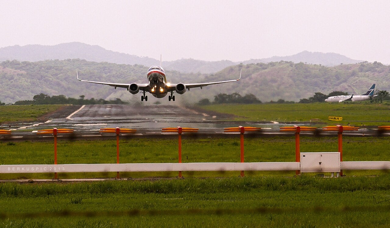 An American Airlines Boeing 737 lifts off from the runway at Guanacaste Airport in Liberia, Costa Rica, with green hills behind it.