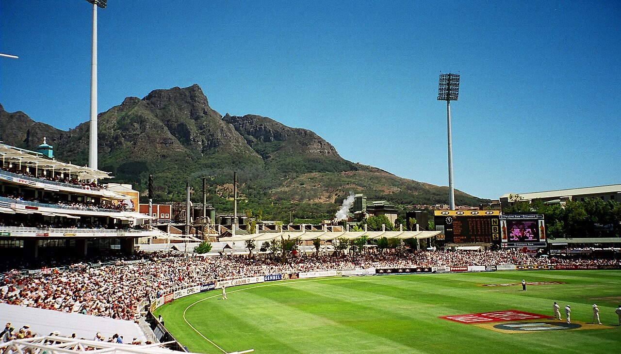 Crowded stands at Newlands cricket ground in Cape Town during a Test match, with the mountain behind the stadium and fielders in white on the green outfield.
