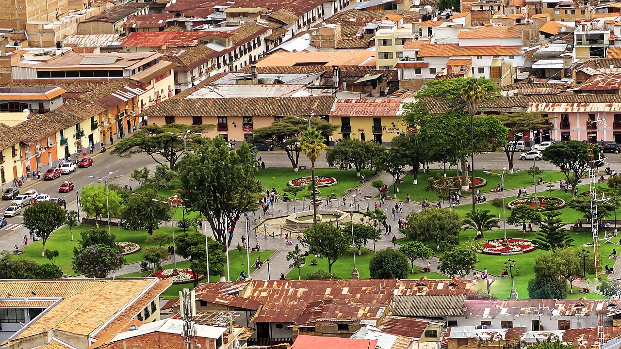 Elevated view of a green town square with a fountain, palm trees and flower beds, surrounded by tiled roofs and colonial buildings