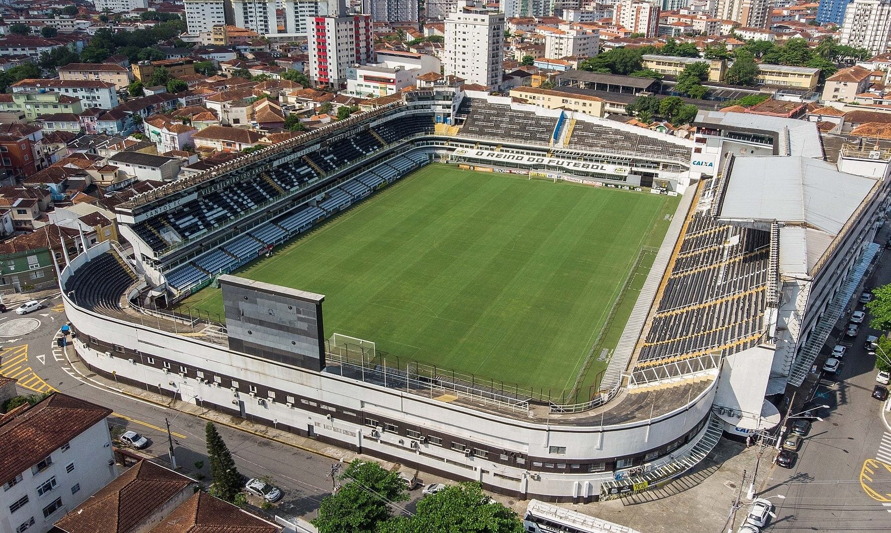 Aerial view of the Vila Belmiro football stadium in Santos, with the green pitch, curved white outer wall and surrounding houses and apartment blocks