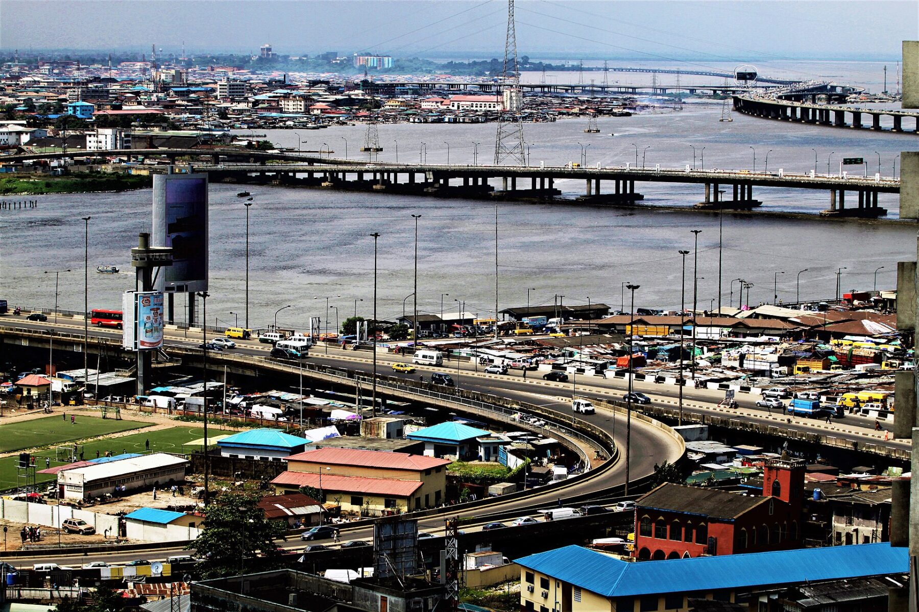 Aerial view of the bridges linking Lagos Island and the mainland across the lagoon, with a curving flyover, traffic and rooftops in the foreground