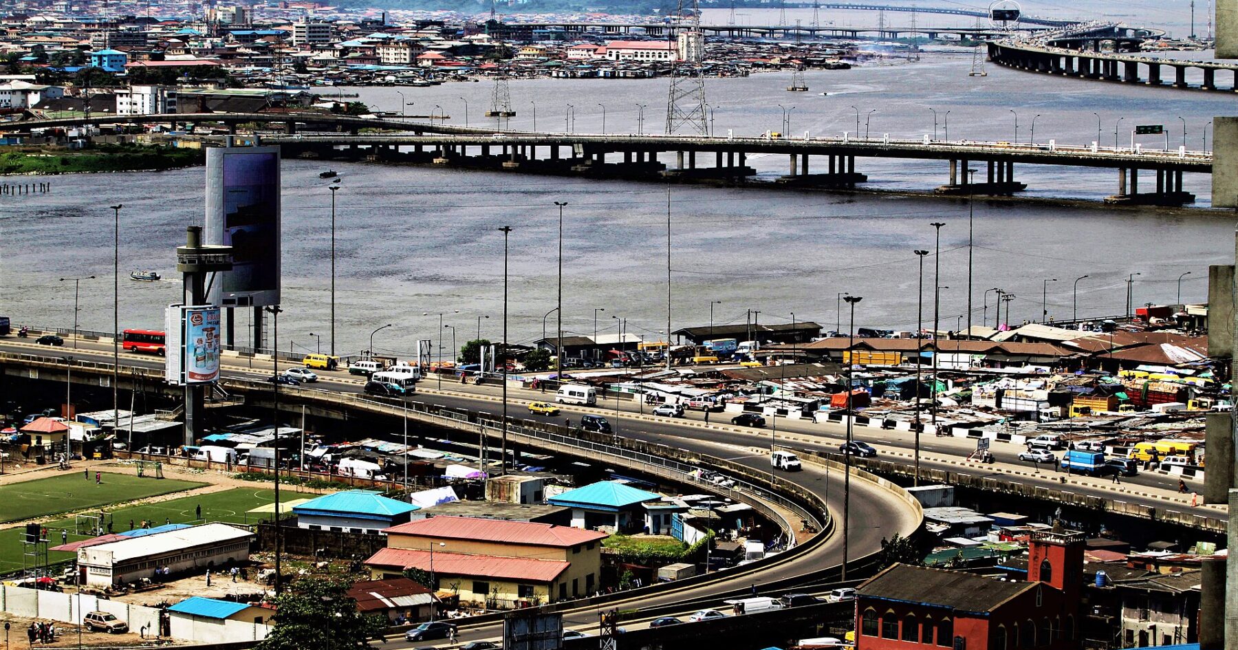 Aerial view of the bridges linking Lagos Island and the mainland across the lagoon, with a curving flyover, traffic and rooftops in the foreground