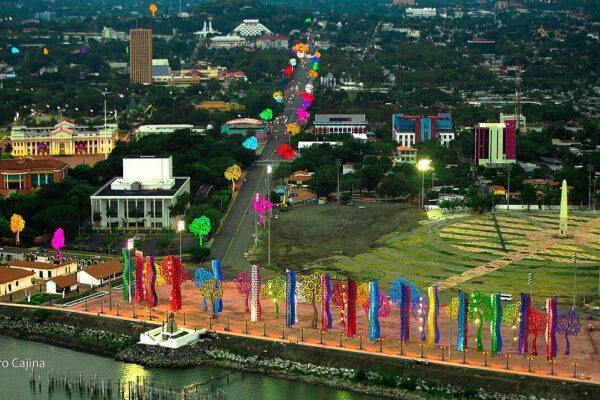 Aerial view of central Managua at dusk, with colourful tree-shaped sculptures along the waterfront and government buildings behind.