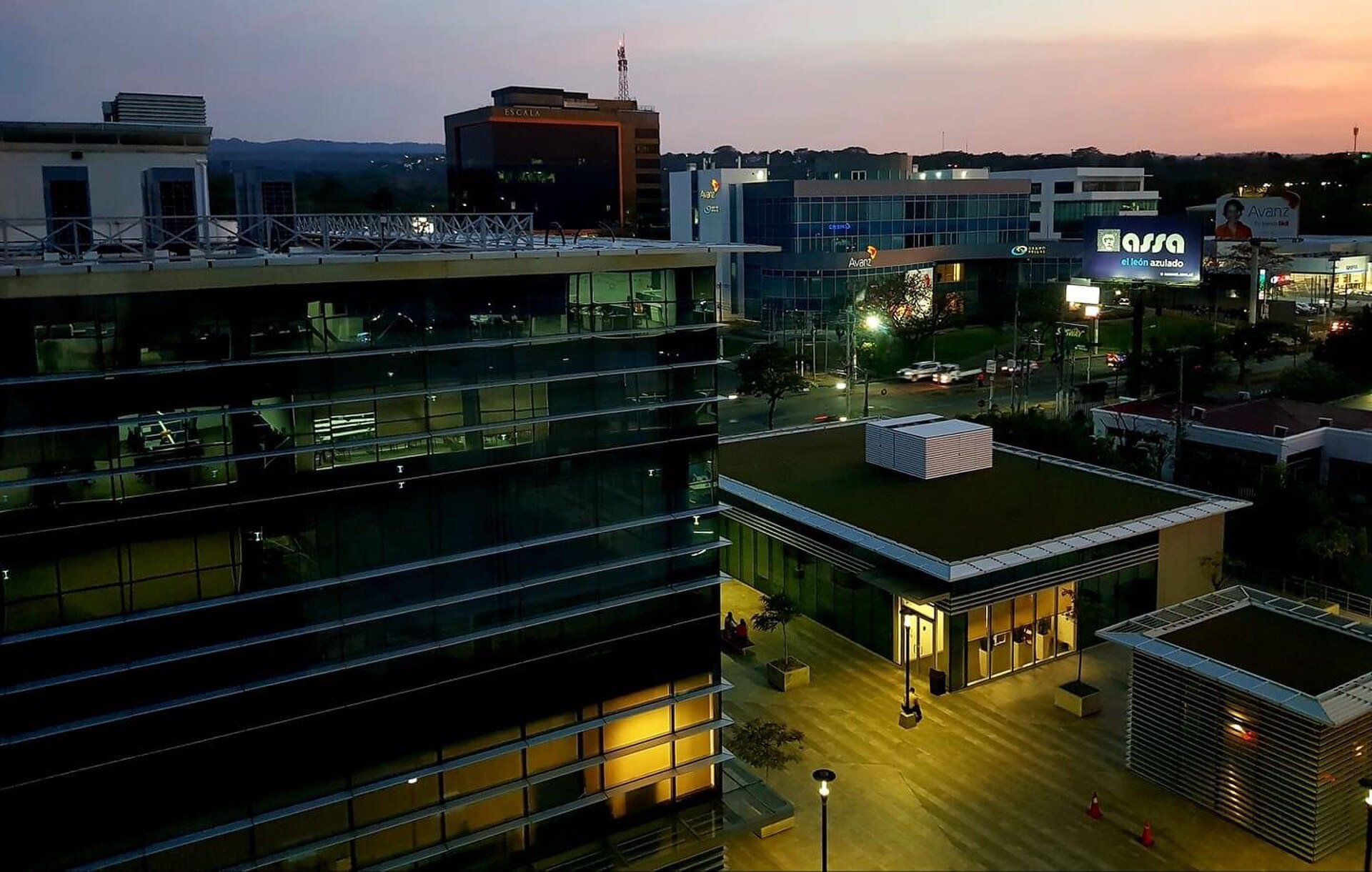 Office buildings in Managua's business district at dusk, with bank and insurance company signs on the street corner
