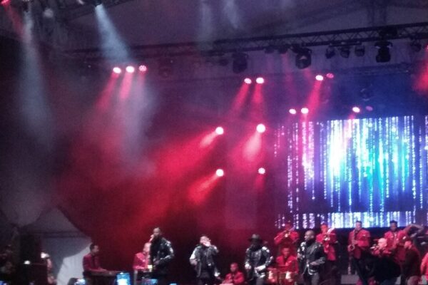 Musicians in red jackets and a horn section perform on a lit stage at the Calle de la Feria street festival in Cali, Colombia