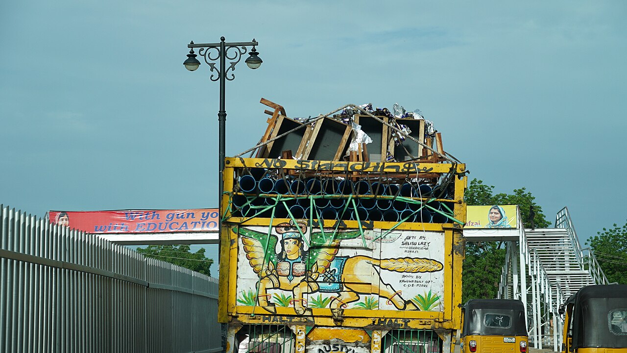 A painted lorry drives under a footbridge in Maiduguri, Nigeria, beside banners showing Malala Yousafzai and an education slogan