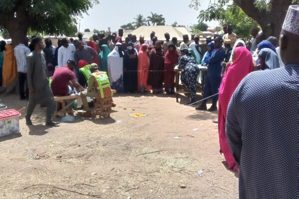 Voters and officials in bright vests gather around a table under trees at a polling unit in Pantami, Gombe, northern Nigeria
