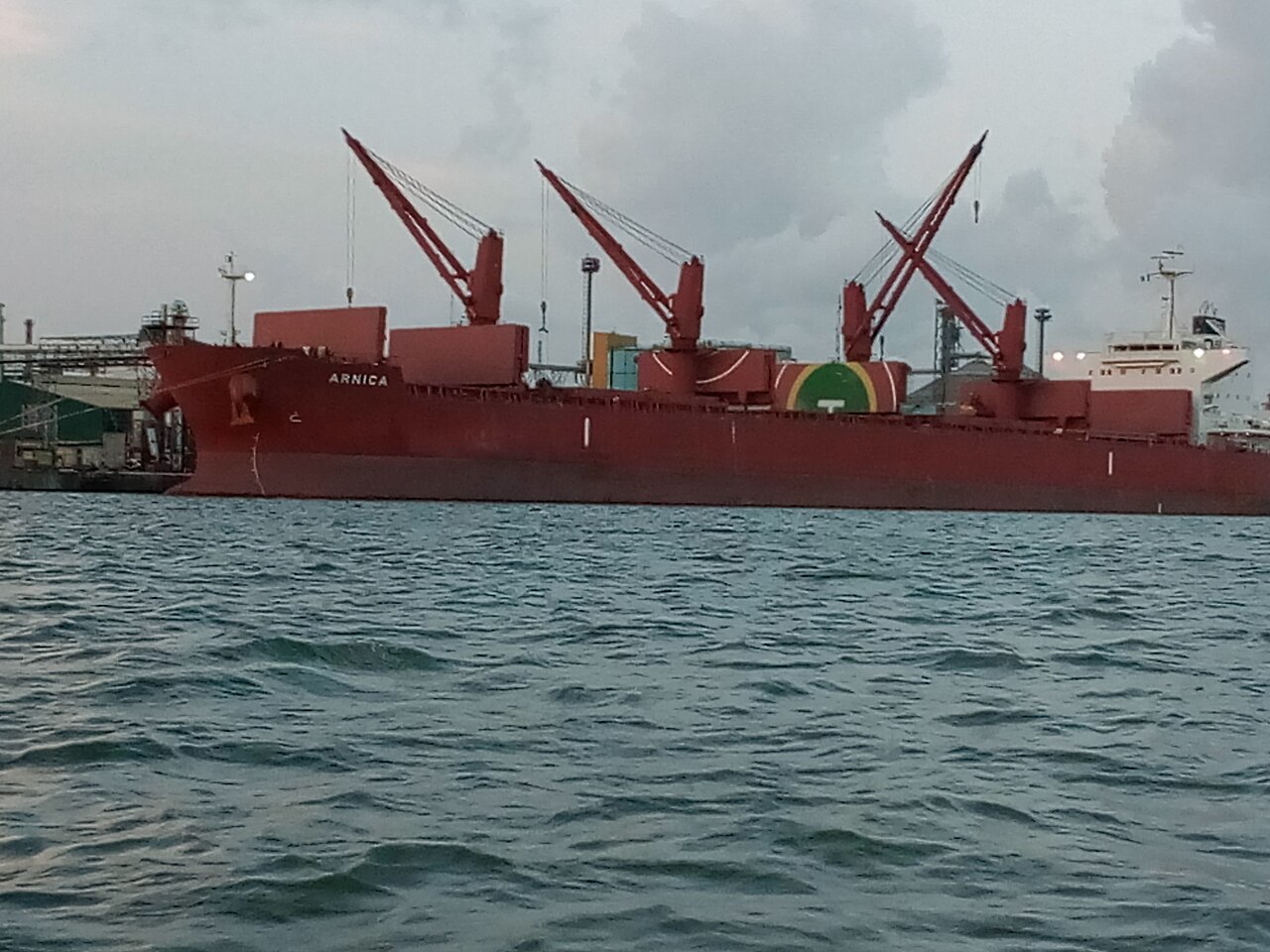 A red bulk carrier with three deck cranes moored at a quay in the Apapa port complex, Lagos, Nigeria