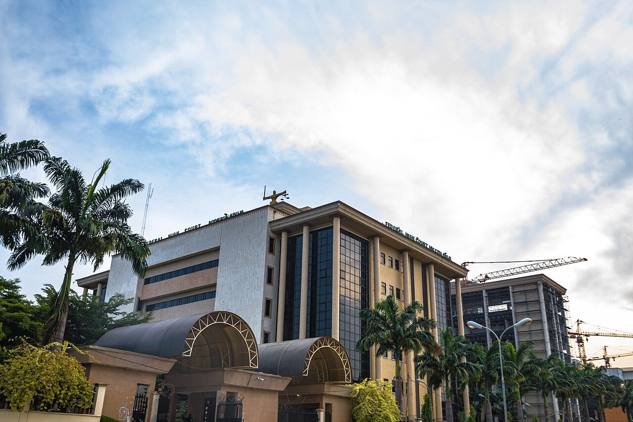 The Federal High Court building in Abuja, a tall beige and glass building with a statue of scales of justice on its roof