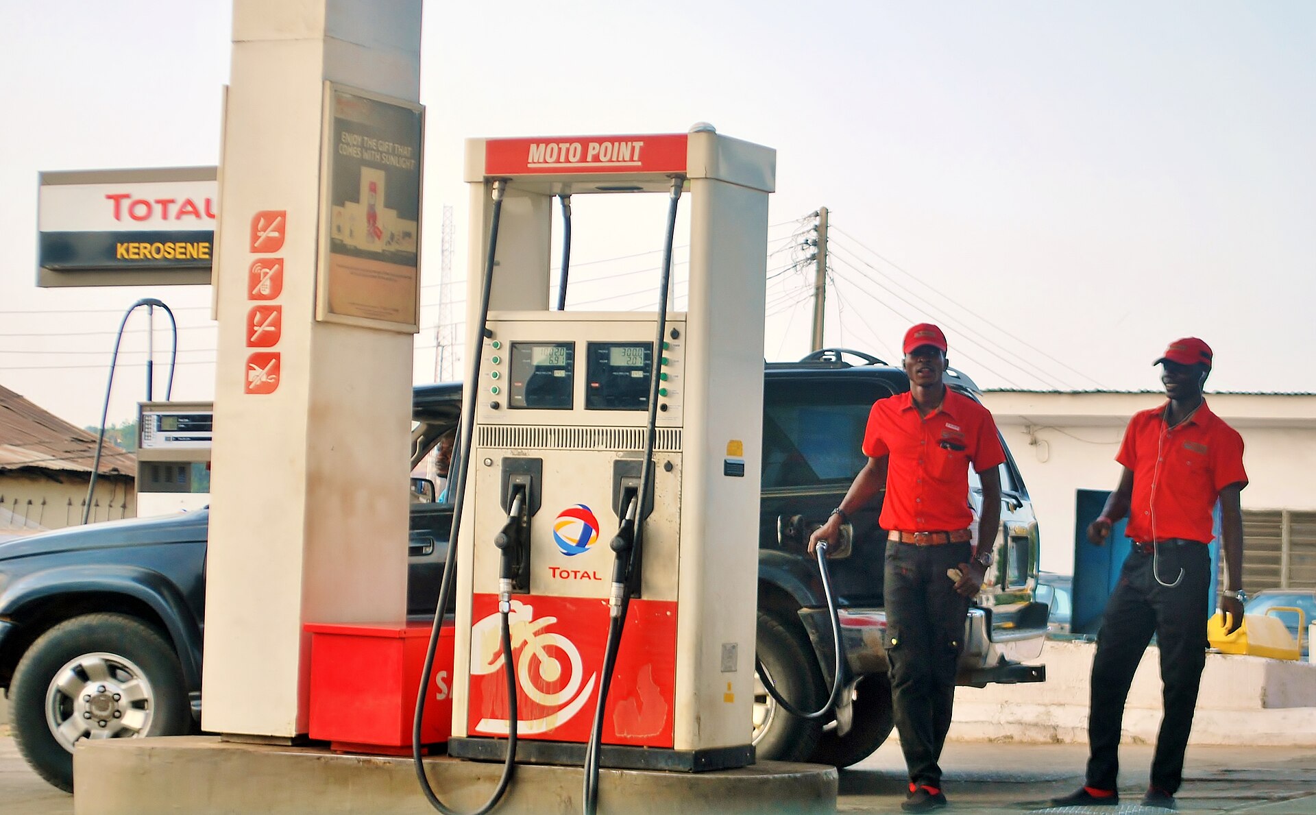Two attendants in red uniforms beside a fuel pump at a petrol station in Ilorin, Kwara State, Nigeria