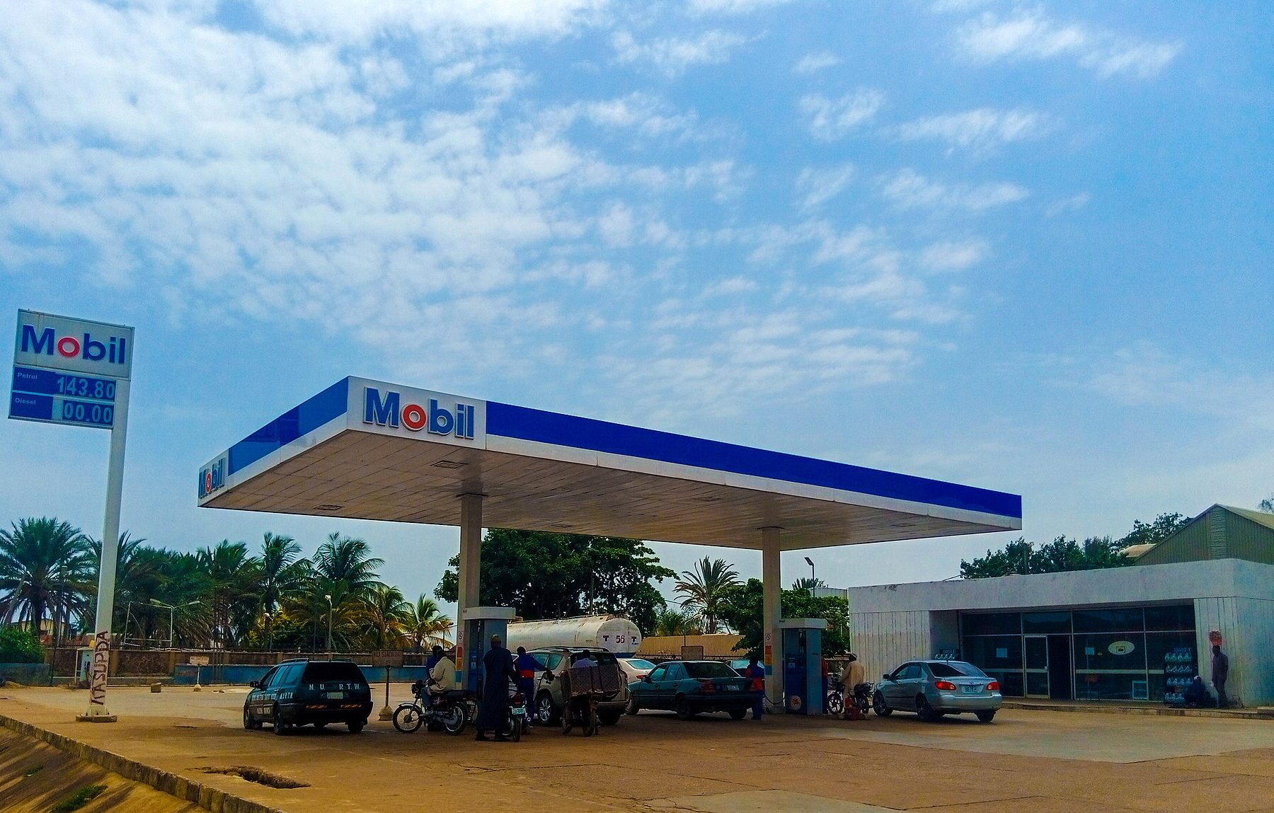 A Mobil-branded filling station with a blue and white canopy, cars and motorbikes on its forecourt, in Nigeria