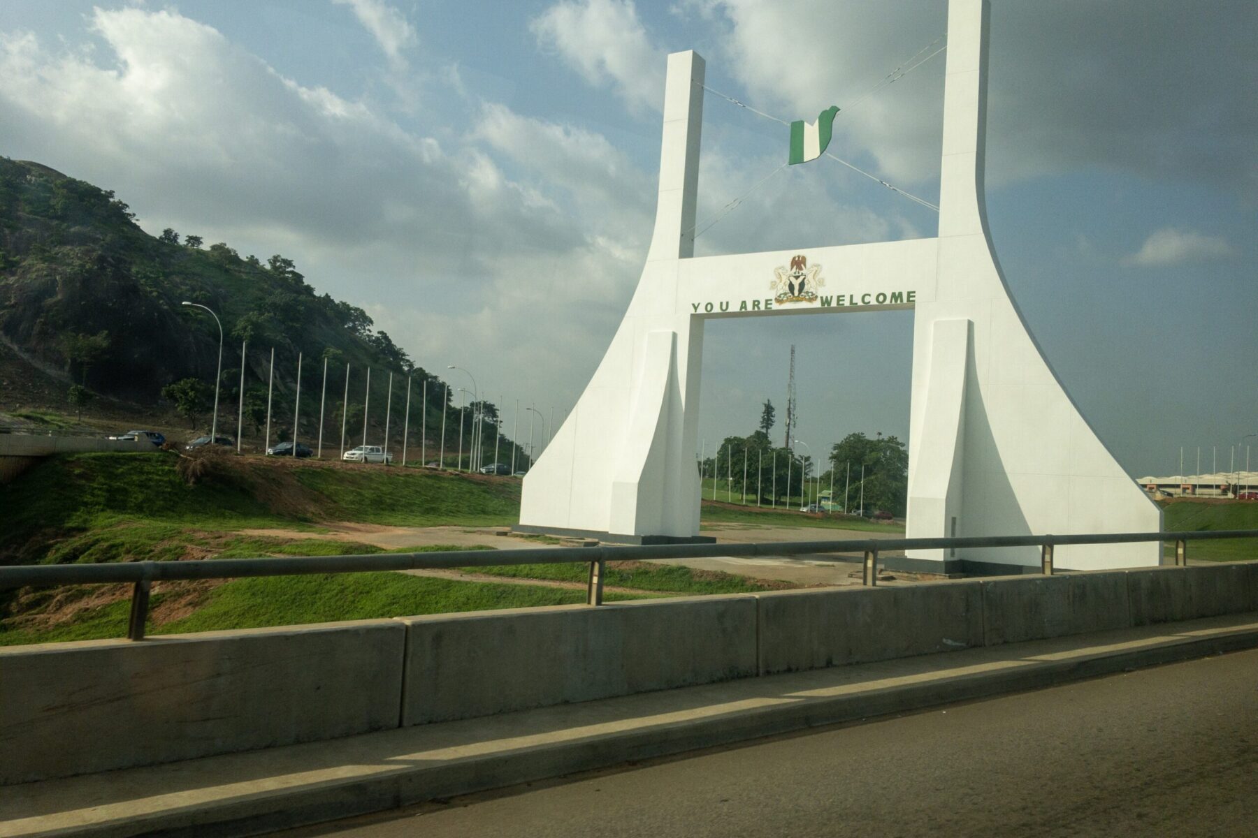 The white 'You Are Welcome' city gate at the entrance to Abuja, Nigeria's capital, with a green hill behind