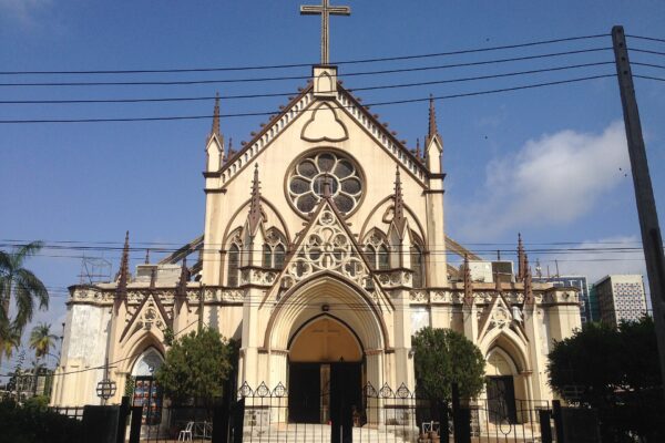 The cream-coloured Gothic-style facade of the Holy Cross Cathedral on Lagos Island under a blue sky, with a cross on top of the gable