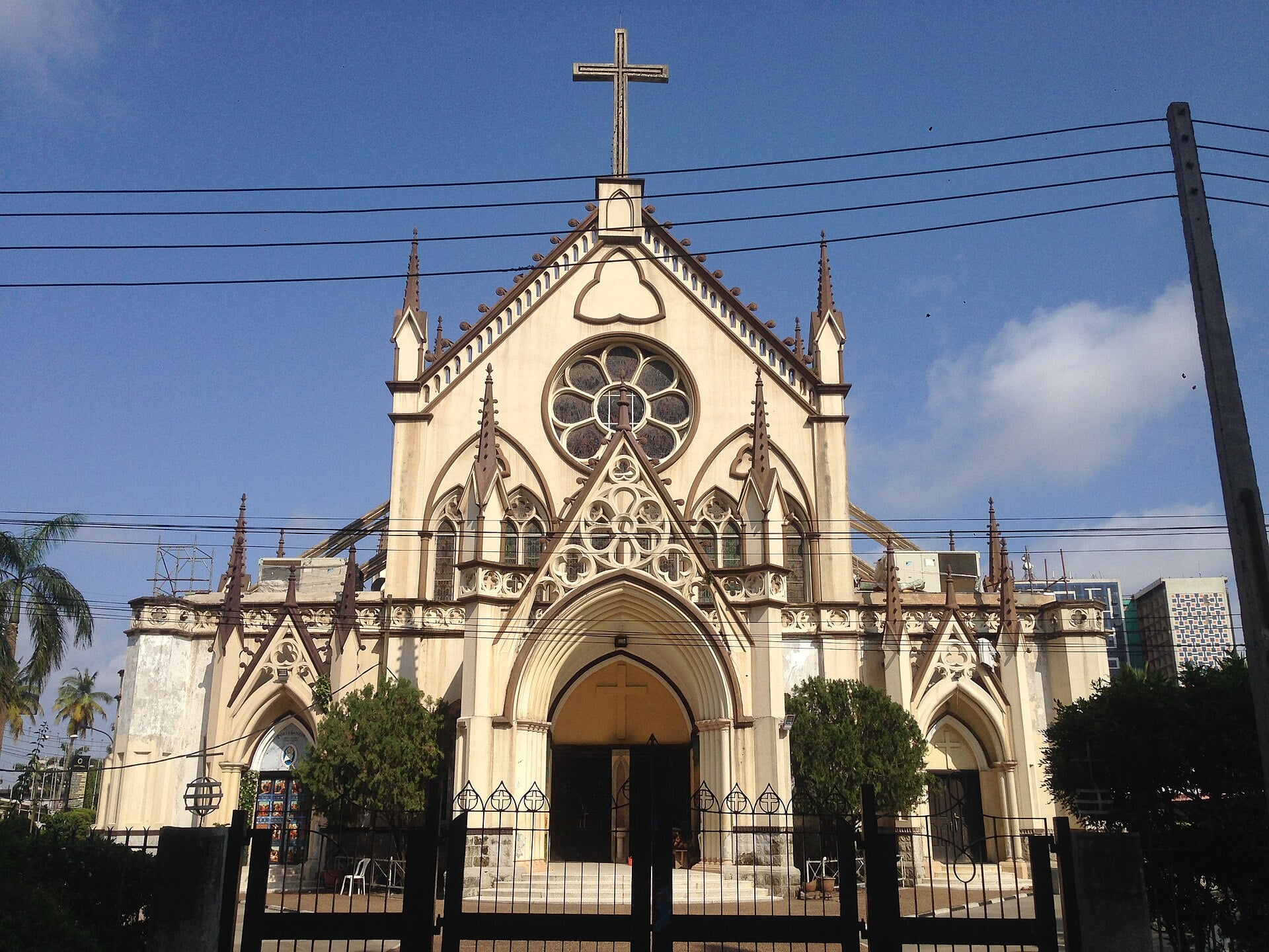 The cream-coloured Gothic-style facade of the Holy Cross Cathedral on Lagos Island under a blue sky, with a cross on top of the gable