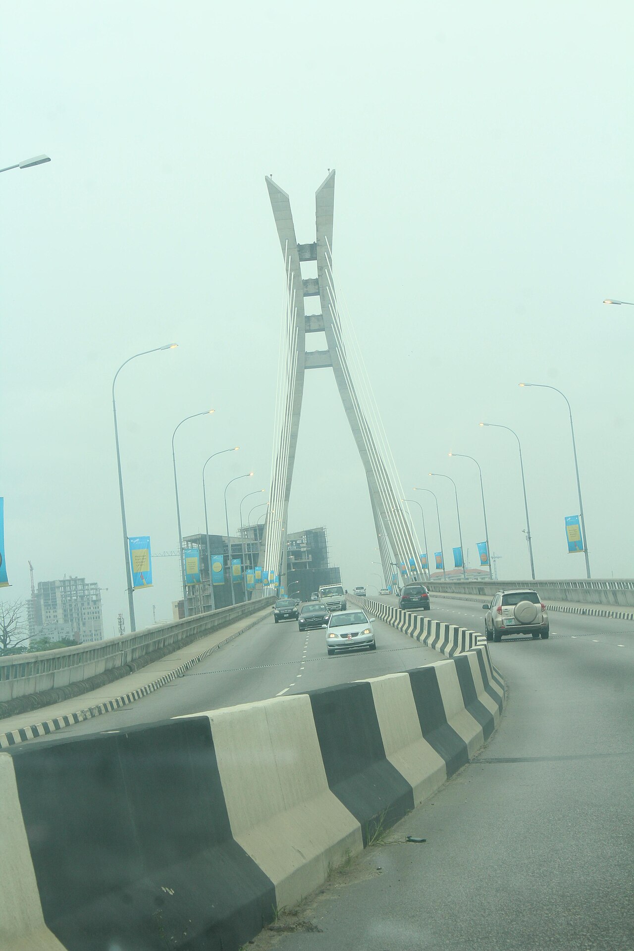 Cars drive over a cable-stayed road bridge with a tall V-shaped tower in hazy Lagos, Nigeria