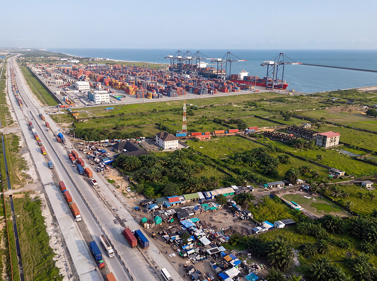 Aerial view of the Lekki Deep Sea Port with container stacks, ship-to-shore cranes, a docked container ship and trucks queuing on the access road