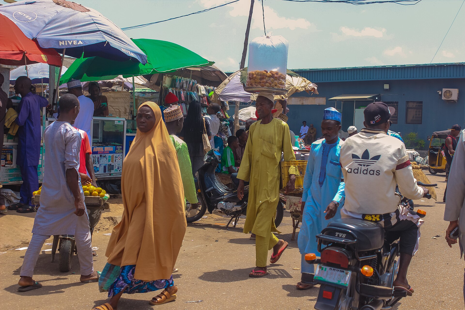 Shoppers and traders walking past stalls and parasols at Kaduna Central Market in northern Nigeria