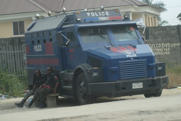 Blue armoured Nigeria Police truck marked RRS with two officers resting on a bench beside it