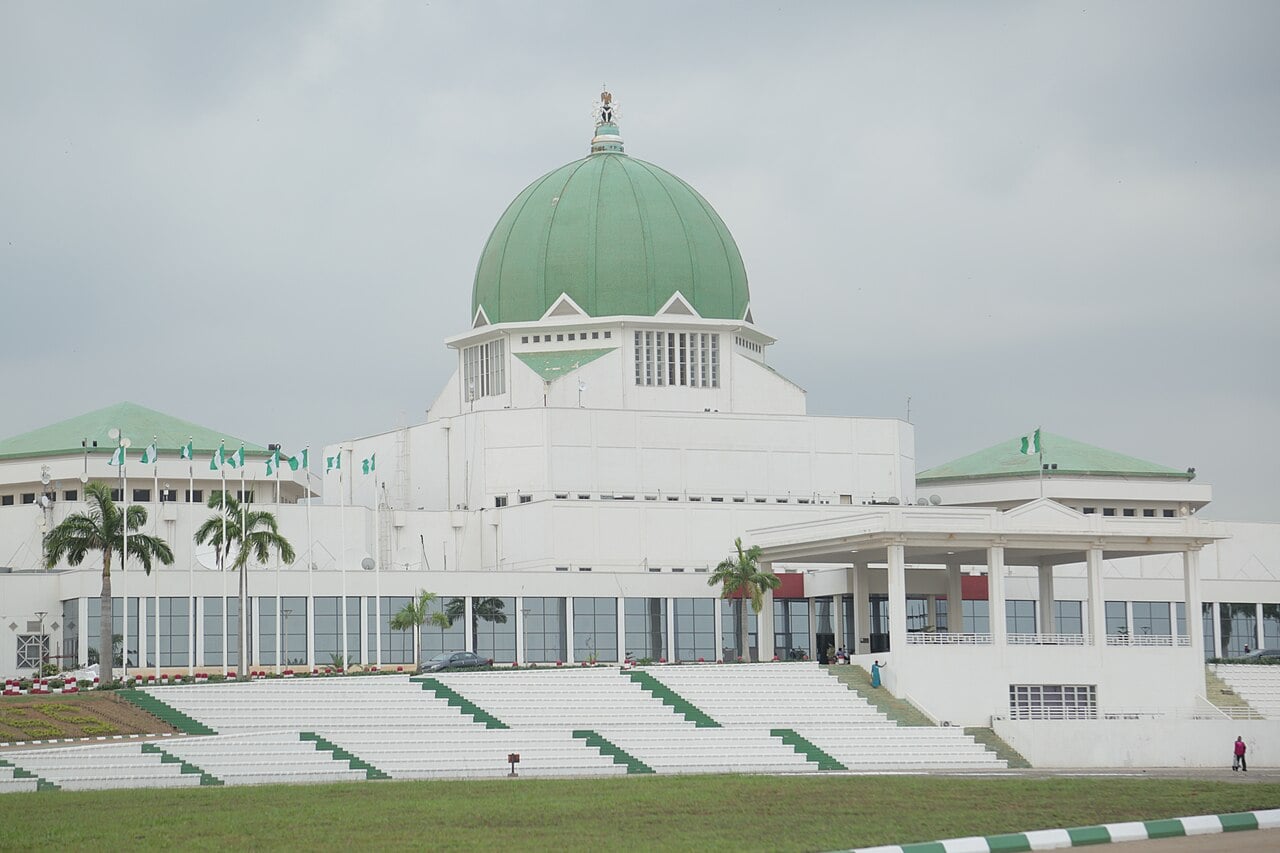 White National Assembly building in Abuja with a green dome, Nigerian flags and palm trees