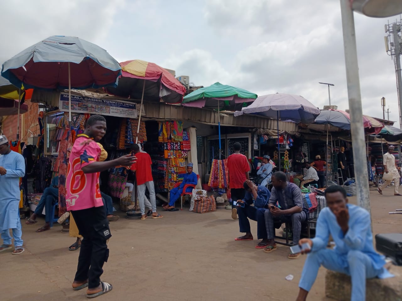 Traders and shoppers under colourful umbrellas in front of fabric stalls at Wuse Market in Abuja