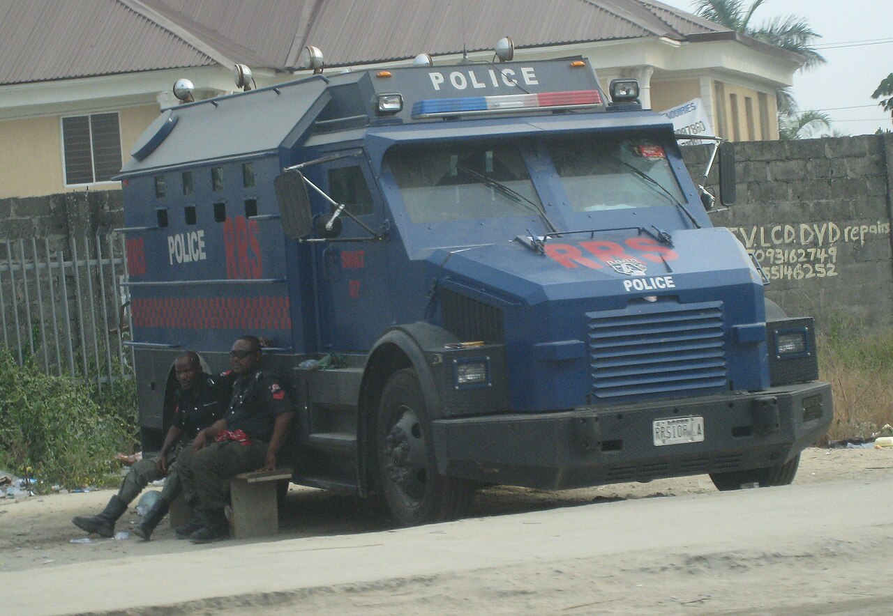 Blue armoured Nigeria Police truck marked RRS with two officers resting on a bench beside it