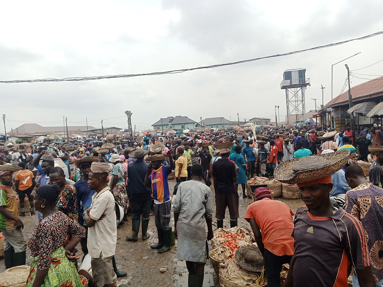Crowd of traders and shoppers, some carrying wide baskets on their heads, among sacks of tomatoes at an open-air market in Lagos