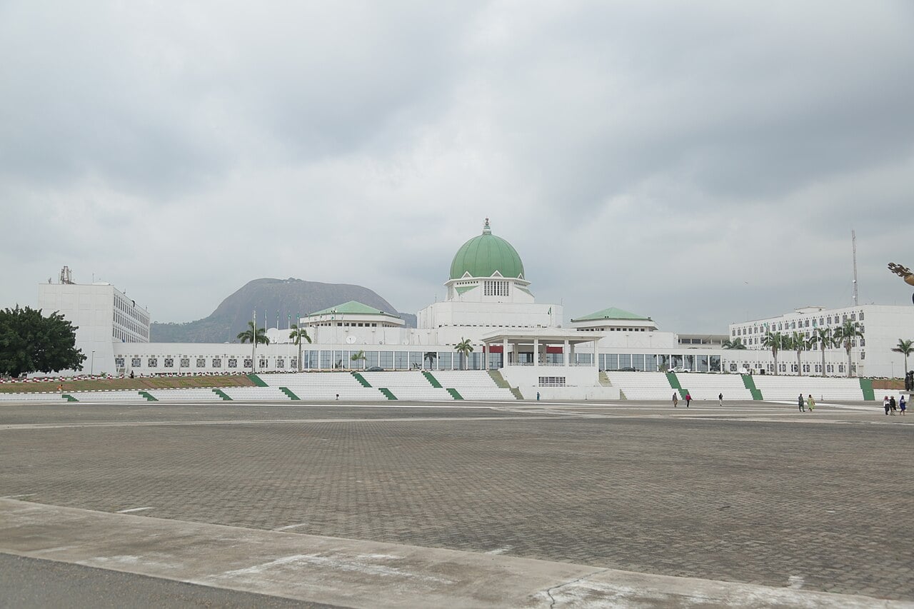 The domed National Assembly complex in Abuja, Nigeria, seen across a paved plaza with Aso Rock behind it