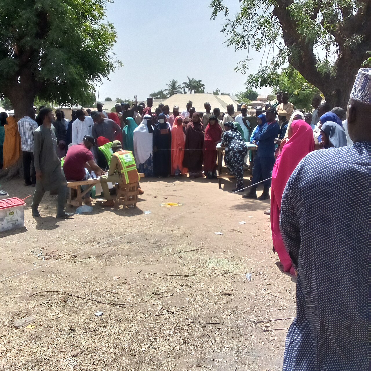 Voters and election officials gather around a table under trees at a polling unit in Pantami, Gombe State, Nigeria